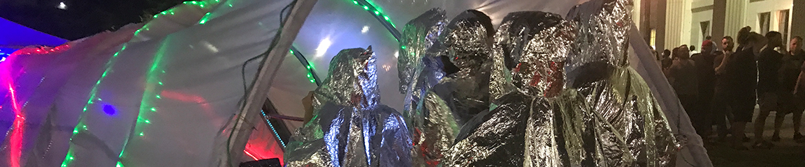 a group of people wearing silver ponchos stepping through a mess tunnel