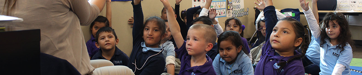 a group of children raising their hand in an elementary classroom